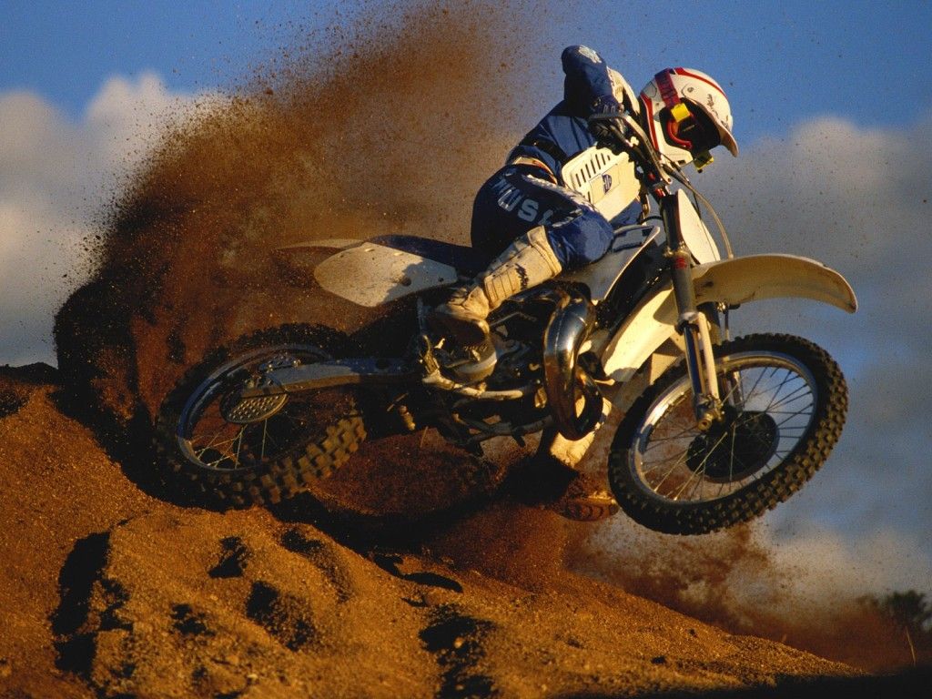 Man on a dirt bike, long tail of sand behind him.